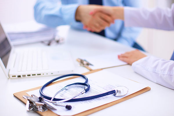 Male and female hands shaking with laptop and stethoscope