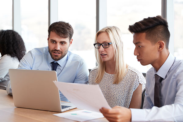 Female and two males looking at paper and laptop