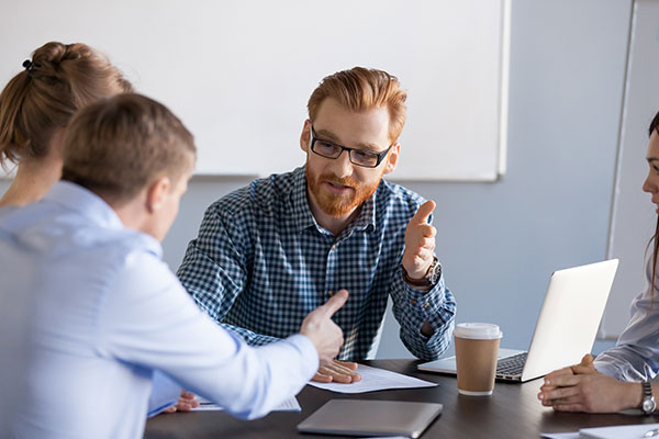 Two males and two females at conference table with laptop and coffee