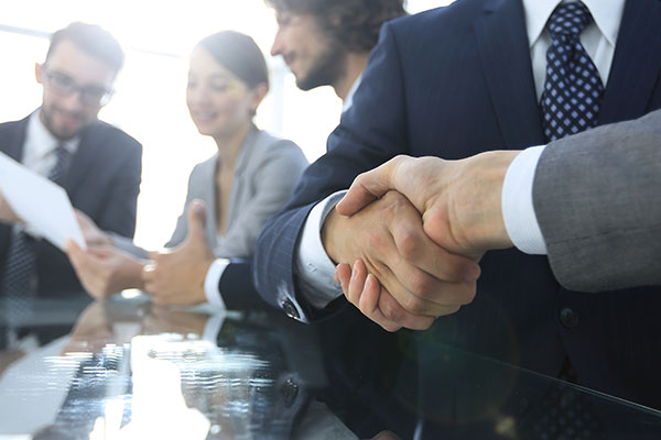 Female and four males at conference table with handshake