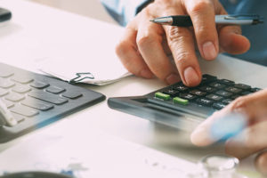 typing into a calculator on a desk with papers and and tablet