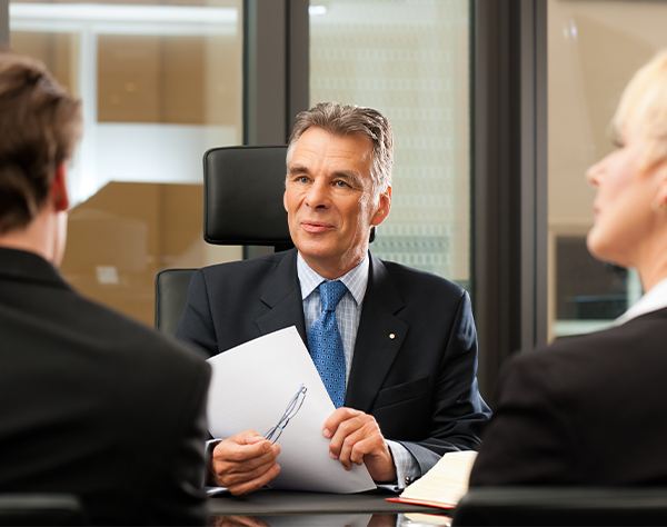 Two clients sitting at arbitration with arbiter pointing at paperwork